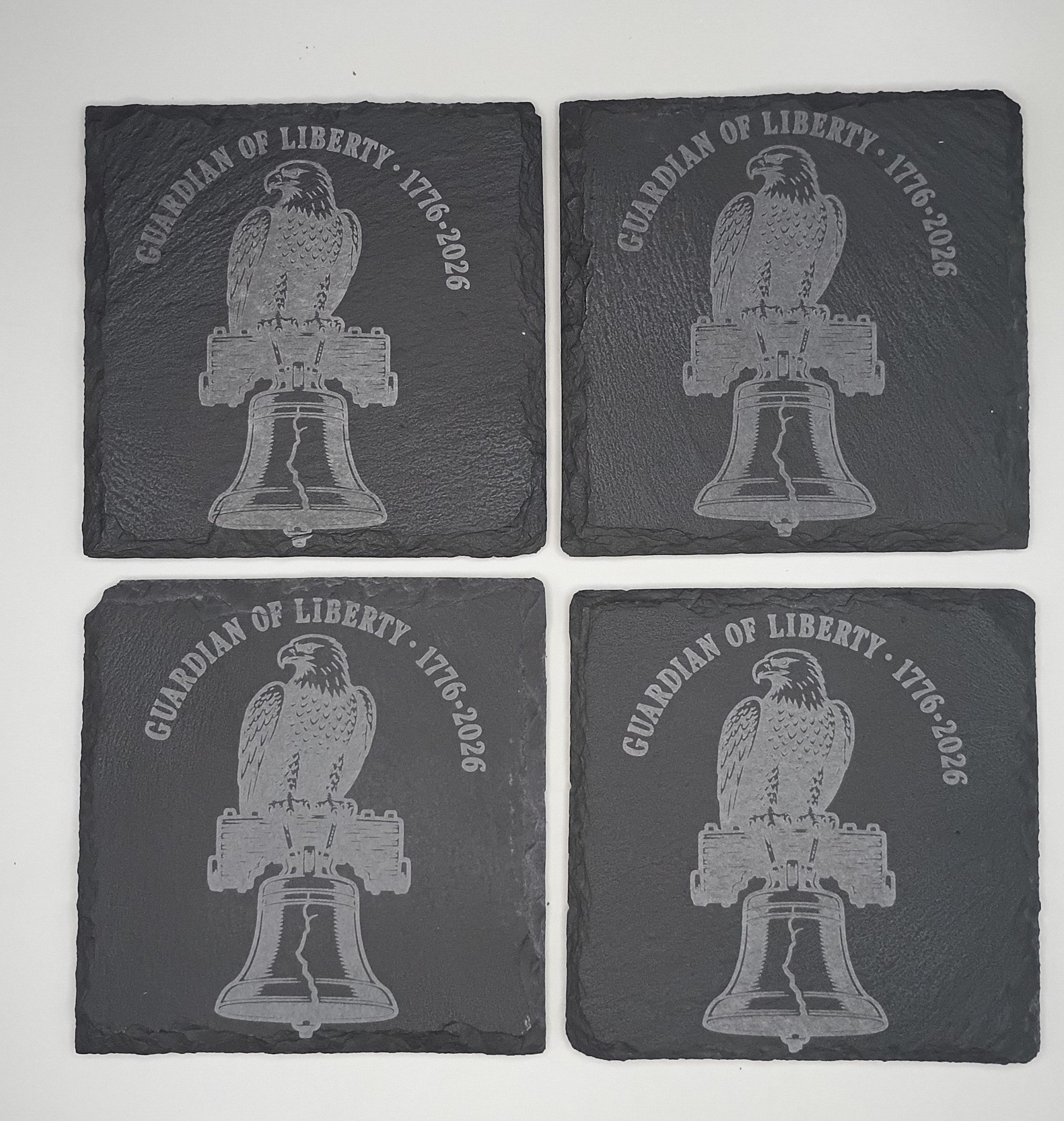 Four slate coasters with engraved eagle and bell design on a white background