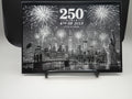 Decorative plaque with fireworks and cityscape design celebrating the 250th anniversary of the 4th of July.